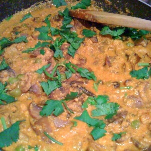 Mushroom Mutter Masala cooking in a pan, being stirred with a wooden spoon