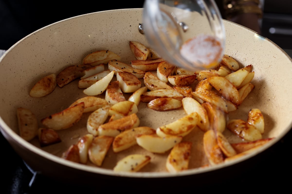 adding spices to the potatoes in the pan
