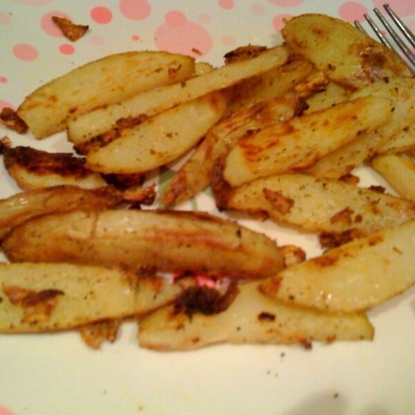 Close up of baked garlic cajun fries on a white plate, a fork in the background