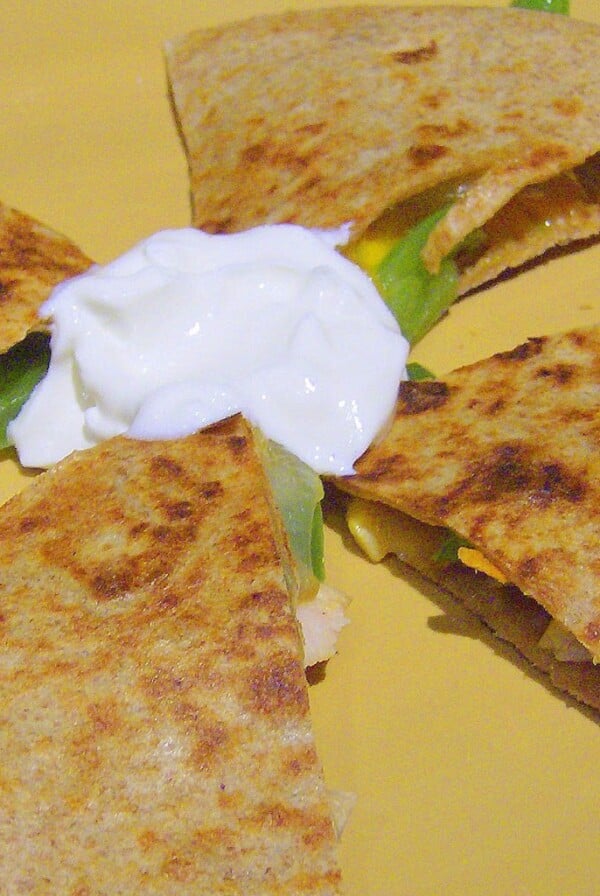 A grilled veggie quesadilla cut into quarters with sour cream in the centre. Placed on a yellow plate