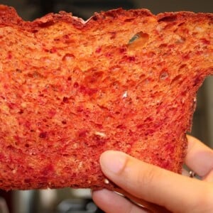 A slice of beetroot bread with orange zest being held up towards the camera