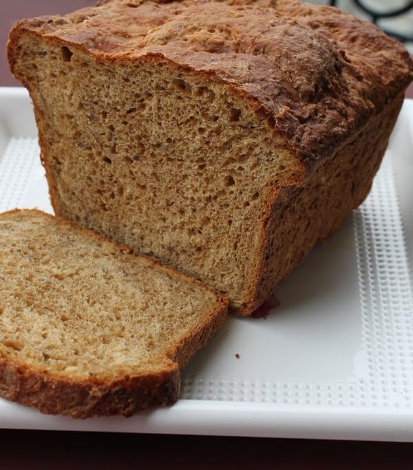 A loaf of greape oats flaxseed wheat bread on a white plate with the end sliced off