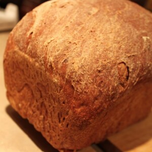 A loaf of Blueberry Apple Wheat Bread on a wooden chopping board