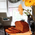 A loaf of date maple wheat bread cut into slices next to a bunch of flowers