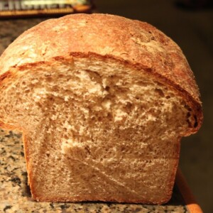 A loaf of wheat oat flax bread cut in half on a work surface