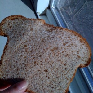 A slice of strawberry ice cream loaf being held towards the camera