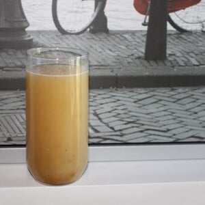 A glass of apple panna on a window sill with cobblestone paving outside
