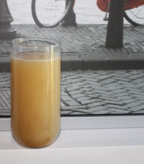 A glass of apple panna on a window sill with cobblestone paving outside