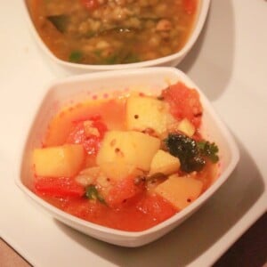 A potato in tomato curry served in a bowl on a white plate