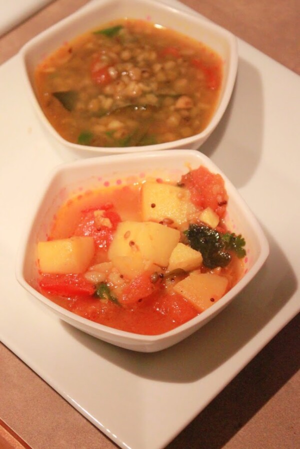A potato in tomato curry served in a bowl on a white plate