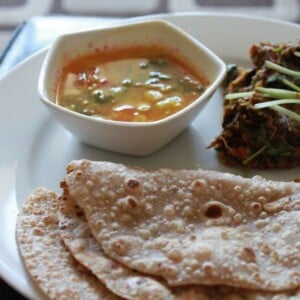Baingan Bharta, sambhar, roti and papad sweved together on a white plate
