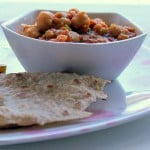 A bowl of chana masala served with roti on a white plate