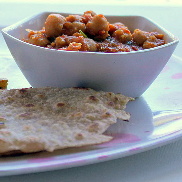 A bowl of chana masala served with roti on a white plate