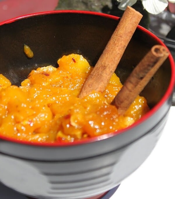 A bowl of mango chutney with two cinnamon sticks
