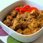 A spinach tomato curry in a white bowl with red pepper garnish