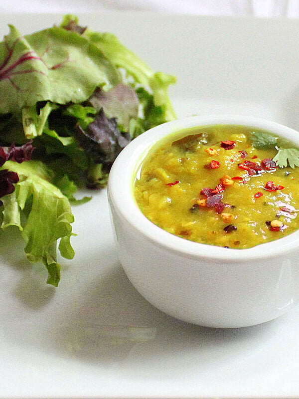A small white bowl of yellow lentil soup served with salad