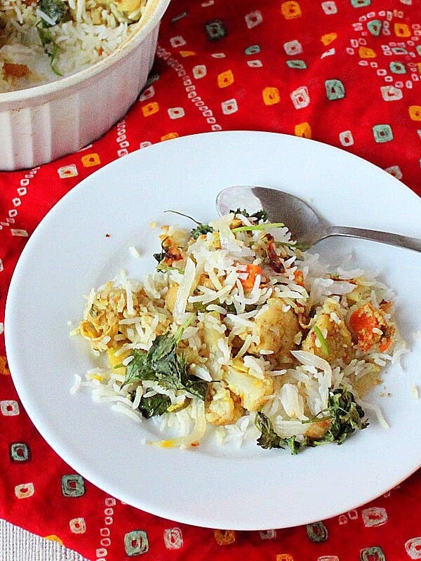 A white plate with layered rice and veggies on a red fabric