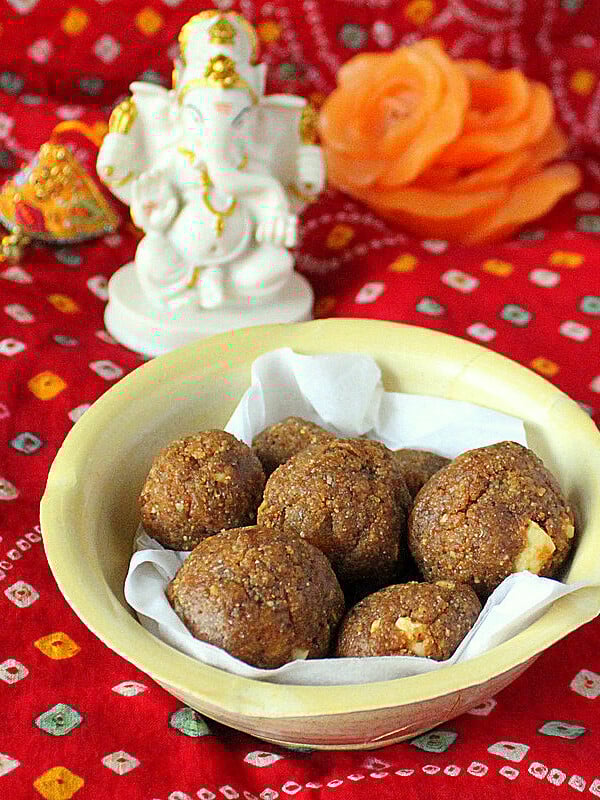 Besan laddoo in a pale bowl on a red background