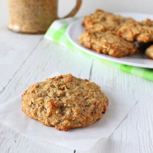 A quinoa raisin muffin cookie on a piece of parchment with a plate of cookies in the background