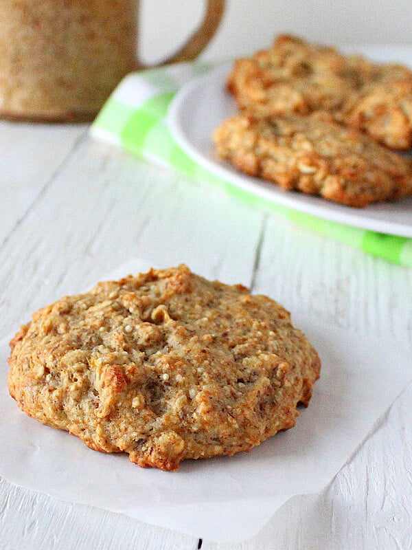 A quinoa raisin muffin cookie on a piece of parchment with a plate of cookies in the background