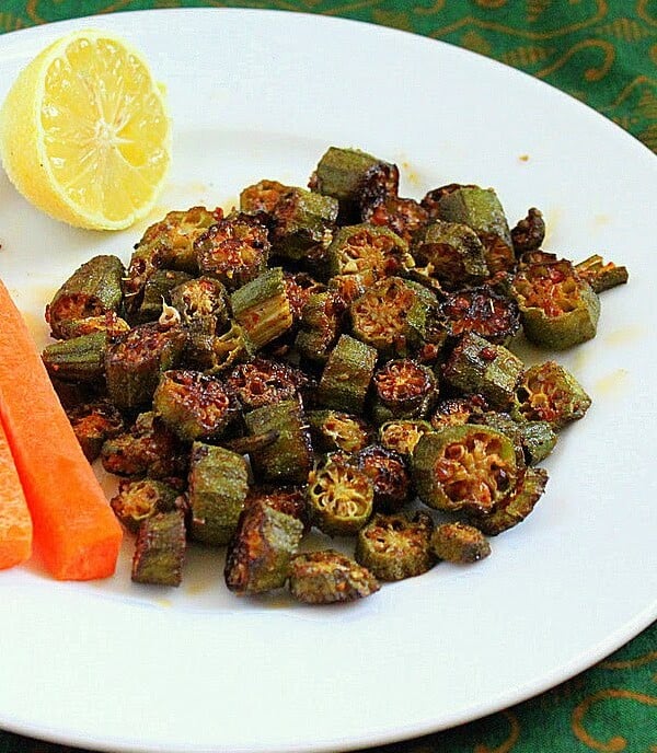 Crisp okra on a white plate werved with a lemon wedge and carrot sticks