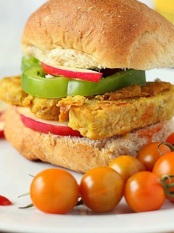 A tempeh frutter in a burger bun served with cherry tomatoes