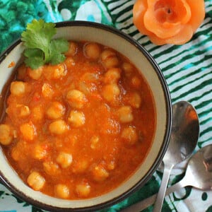 A bowl of vegan Chana Masala on a green cloth, garnished with cilantro