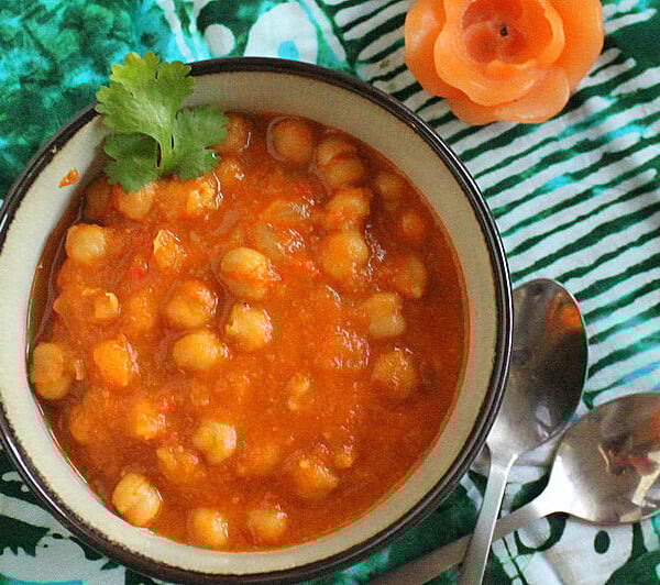 A bowl of vegan Chana Masala on a green cloth, garnished with cilantro