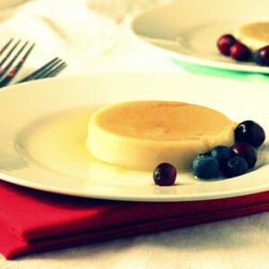 A caramel custard pudding on a white plate served with blueberries