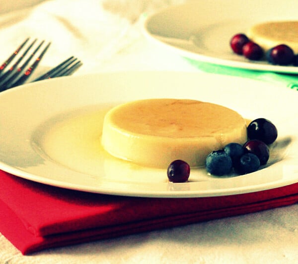 A caramel custard pudding on a white plate served with blueberries