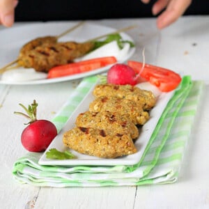 Tempeh Seekh Kebabs on a white serving plate with vegetable garnishes
