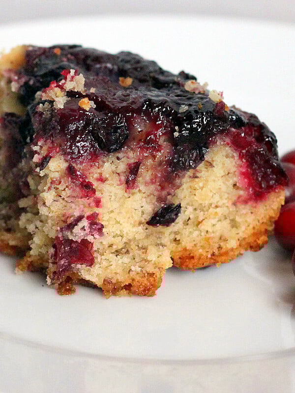 A cranberry and blueberry upside down cake served on a white plate with fresh cramberries