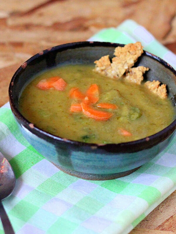 A bowl of Carrot Celery Leek Potato Soup on top of a checked green cloth