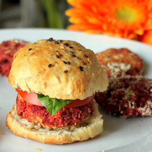 A vegan burger slider on a white plate with an orange flower in the background