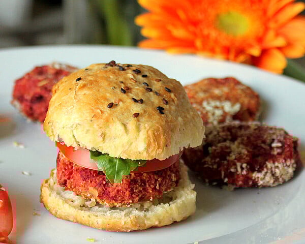 A vegan burger slider on a white plate with an orange flower in the background