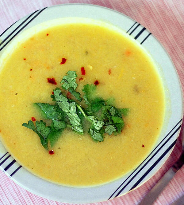 A bowl of carrot leek parsnip soup garnished with green leaves