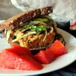 A tempeh sandwich on a white plate with red garnish