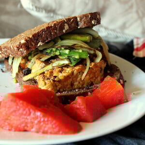 A tempeh sandwich on a white plate with red garnish
