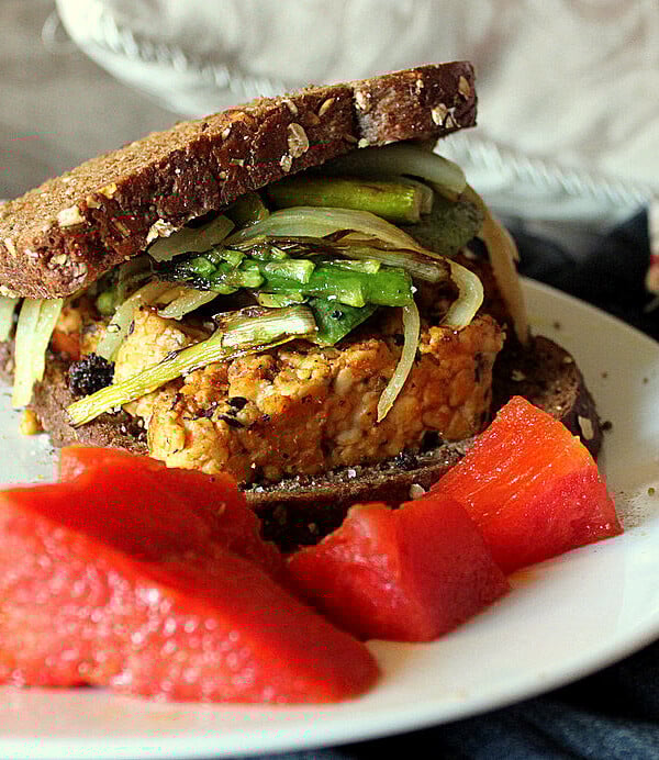 A tempeh sandwich on a white plate with red garnish