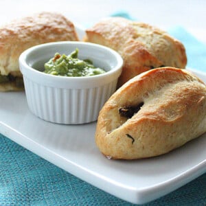 Stuffed pretzels served on a white plate with a green dip