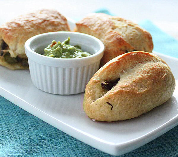 Stuffed pretzels served on a white plate with a green dip