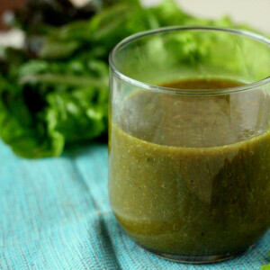 A green smoothie in a short glass, on a light blue background