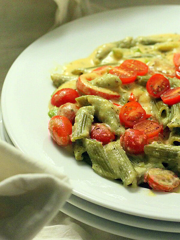 A white shallow bowl, filled with Spinach Penne with Red Bell peppers