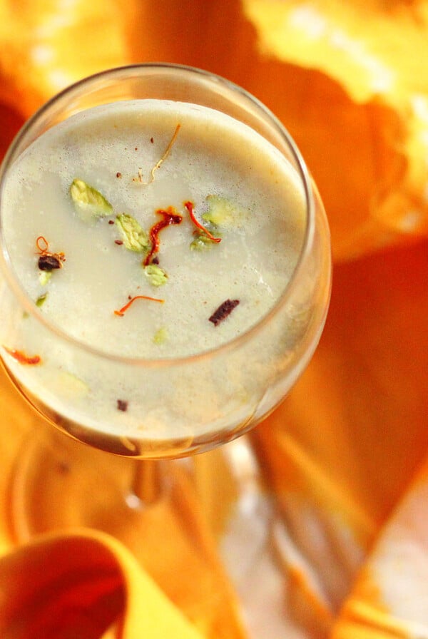 An overhead shot of a glass of thandai on an orange fabric background