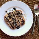 A slice of french toast on a white plate, drizzled with chocolate