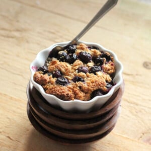 A ramakin on a woooden work surface with Baked French Toast in it. A spoon sticking out of the crisp