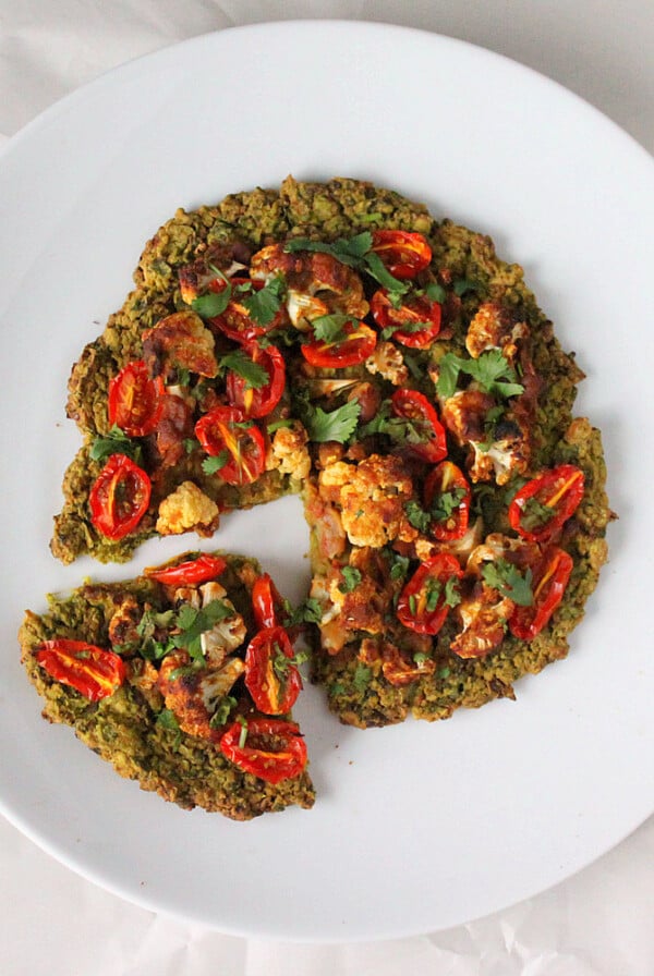 A quinoa chickpea pizza crust on a white plate with a slice taken out