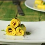 Three khandvi rolled up on a white plate and sprinkled with herbs
