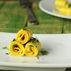 Three khandvi rolled up on a white plate and sprinkled with herbs