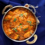 Paneer butter masala served in a siver dish, on a blue background